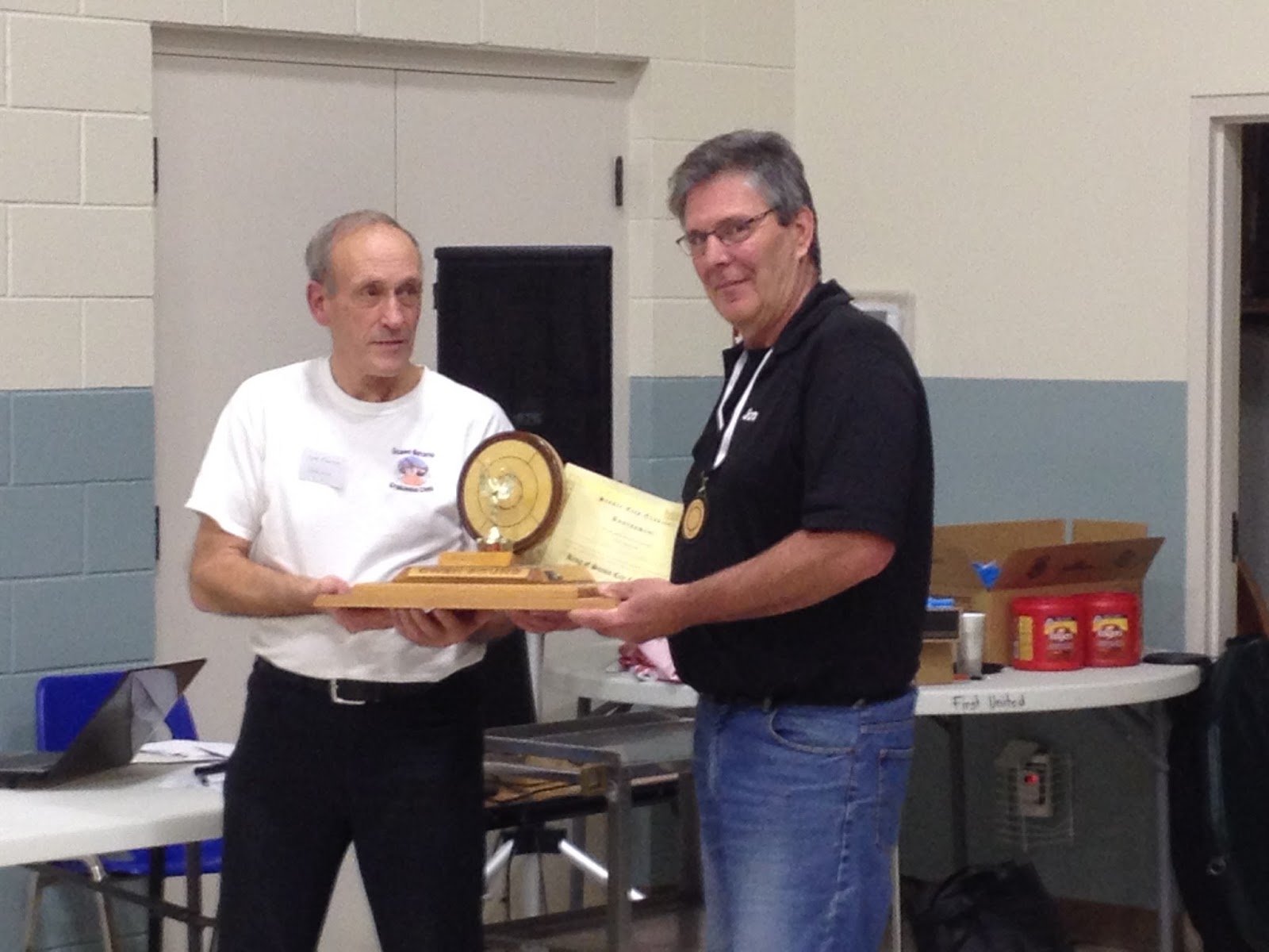 Jon Conrad (right) accepts the trophy from tournament organizer Clare Kuepfer as 2016 Scenic City King of Crokinole